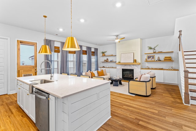 kitchen with white cabinets, dishwasher, light wood-type flooring, decorative light fixtures, and a kitchen island with sink