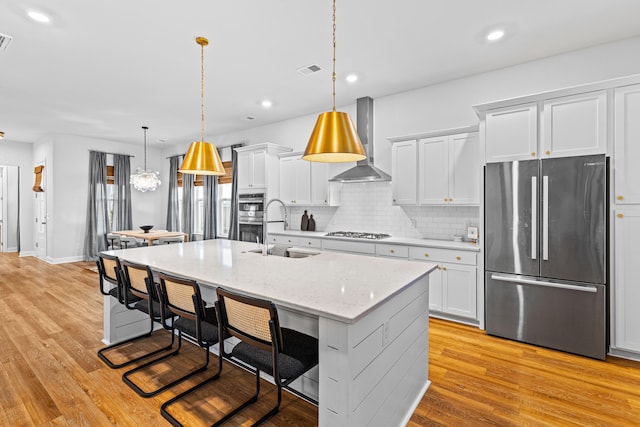 kitchen with stainless steel appliances, sink, wall chimney range hood, and white cabinetry