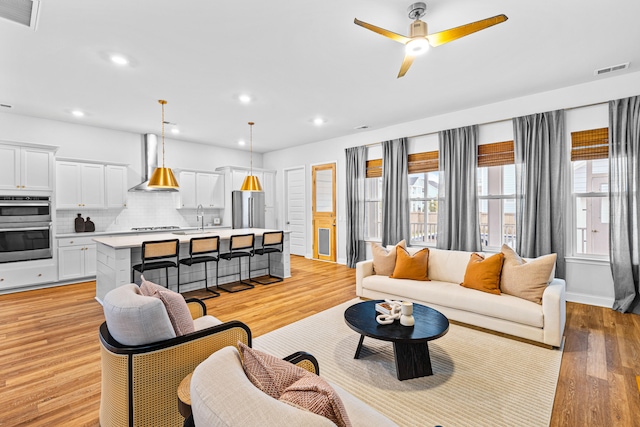 living room featuring light hardwood / wood-style floors, ceiling fan, and sink