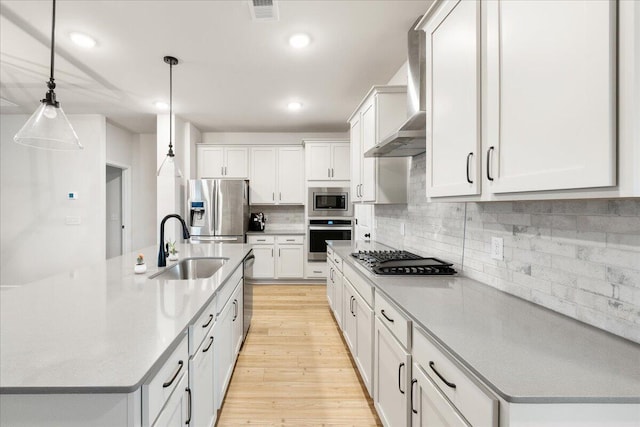 kitchen featuring pendant lighting, white cabinets, light hardwood / wood-style flooring, an island with sink, and appliances with stainless steel finishes