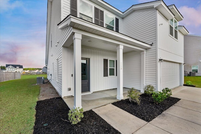 view of front facade featuring a porch, a garage, central air condition unit, and a yard