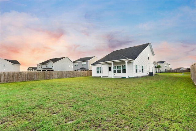 back house at dusk featuring a lawn