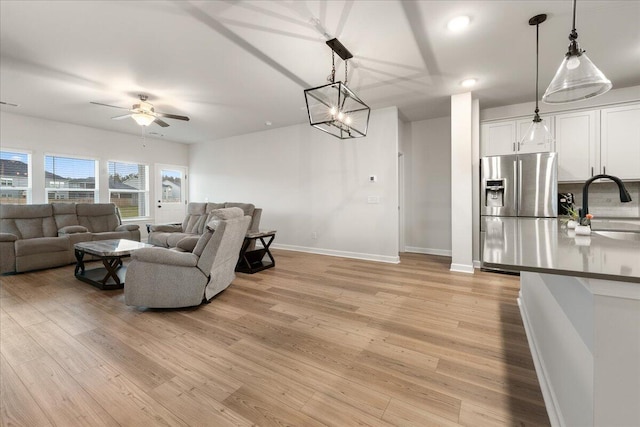 living room featuring light hardwood / wood-style flooring, ceiling fan with notable chandelier, and sink