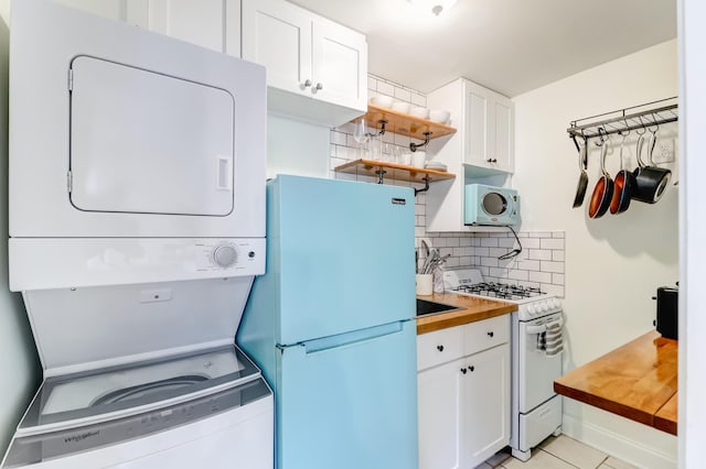 kitchen featuring white cabinets, refrigerator, stacked washer and dryer, and white gas stove