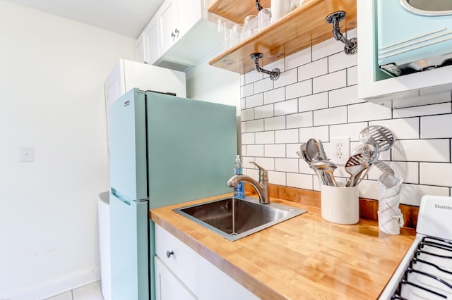 kitchen with wooden counters, sink, light tile patterned floors, tasteful backsplash, and white cabinetry