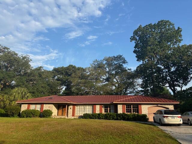 ranch-style home featuring concrete driveway, metal roof, a front yard, and a garage