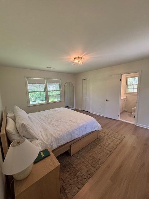 bedroom with baseboards, wood finished floors, and connected bathroom