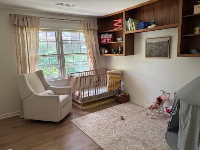 bedroom featuring a nursery area, baseboards, visible vents, and wood finished floors