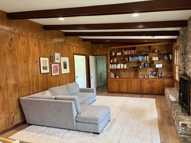 living room featuring light wood-style floors, a brick fireplace, wooden walls, and beamed ceiling