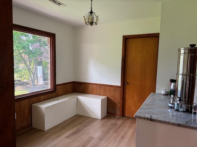 unfurnished dining area with wooden walls, a wainscoted wall, light wood-style flooring, and visible vents