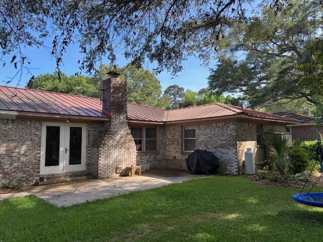 back of property with a patio, french doors, a chimney, brick siding, and a lawn