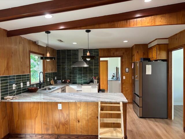 kitchen with a sink, brown cabinetry, wall chimney exhaust hood, freestanding refrigerator, and light wood-type flooring