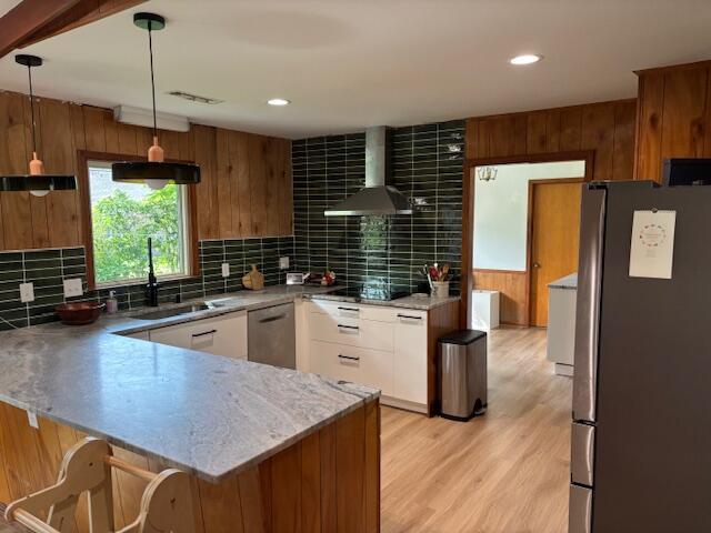 kitchen featuring decorative backsplash, appliances with stainless steel finishes, a sink, a peninsula, and wall chimney exhaust hood