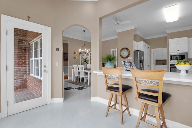 kitchen featuring white cabinetry, a breakfast bar, stainless steel appliances, ceiling fan with notable chandelier, and ornamental molding