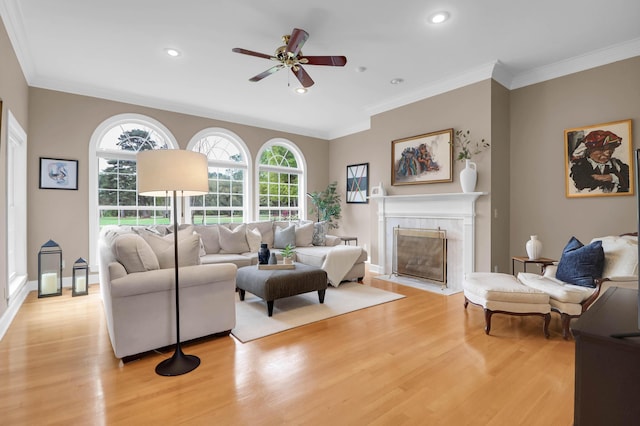 living room featuring a high end fireplace, crown molding, ceiling fan, and light wood-type flooring