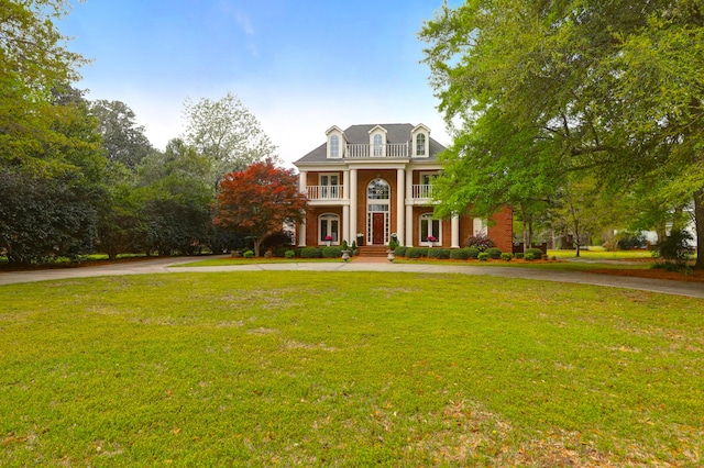 greek revival inspired property with a balcony, a front yard, and curved driveway