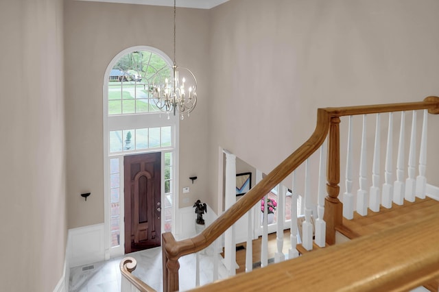 entrance foyer with a decorative wall, stairway, a high ceiling, an inviting chandelier, and wainscoting