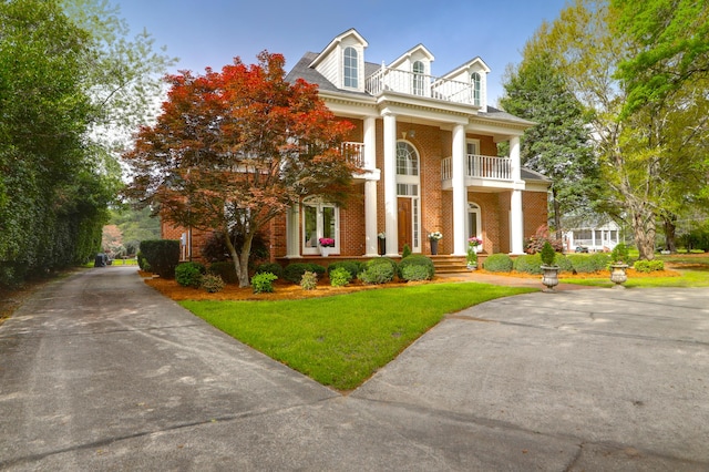 neoclassical home with a balcony, driveway, a front lawn, and brick siding