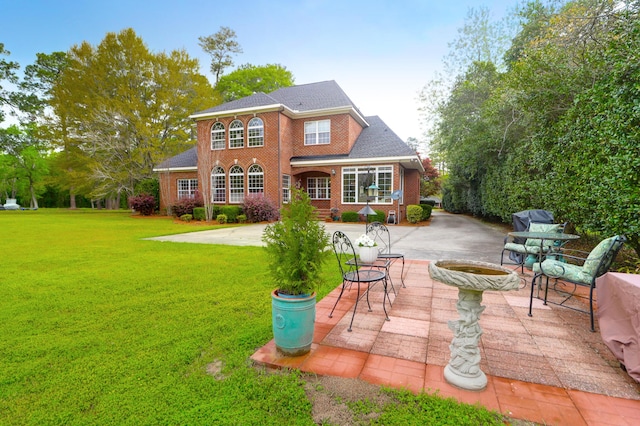 rear view of property with a lawn, driveway, a patio, and brick siding