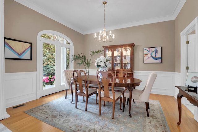 dining area with crown molding, an inviting chandelier, a wainscoted wall, visible vents, and wood finished floors