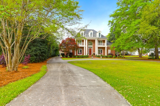 view of front facade featuring a balcony, brick siding, a front lawn, and curved driveway