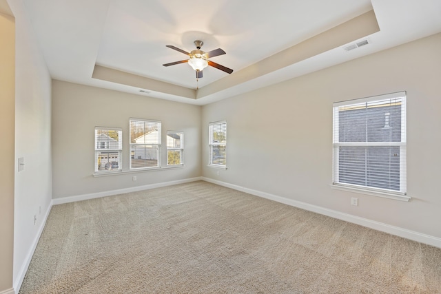 spare room featuring a raised ceiling, ceiling fan, and carpet flooring