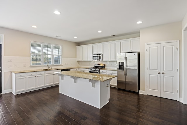 kitchen with white cabinetry, a center island, dark hardwood / wood-style floors, a breakfast bar, and appliances with stainless steel finishes