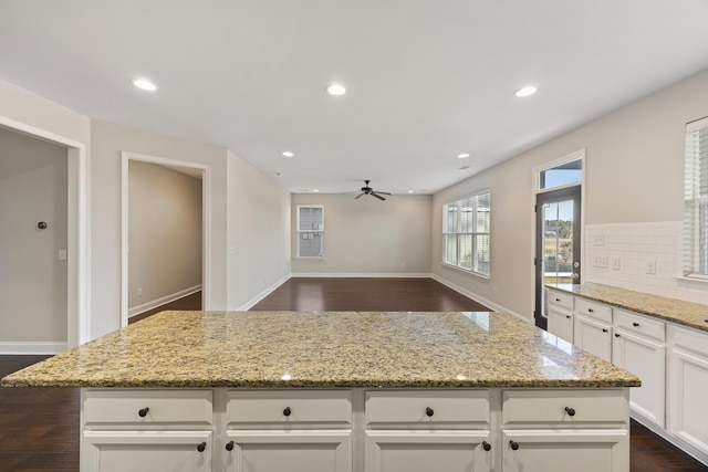 kitchen featuring ceiling fan, a kitchen island, light stone counters, and tasteful backsplash