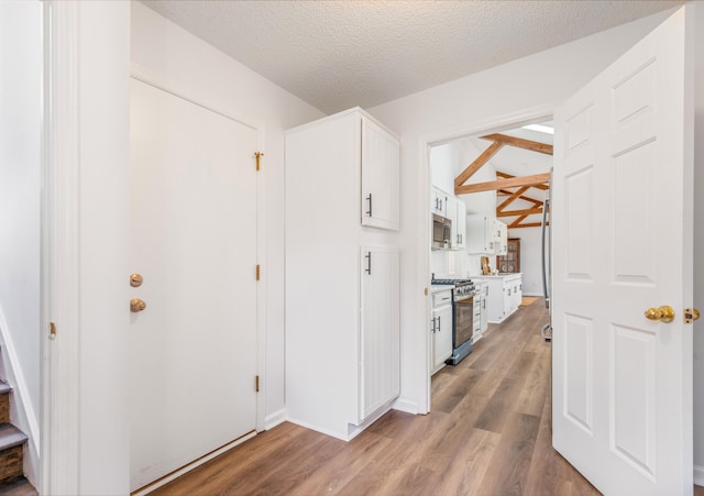 hallway featuring a textured ceiling, light wood-type flooring, and lofted ceiling with beams