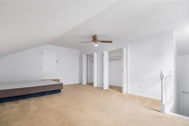 bedroom with two closets, vaulted ceiling, ceiling fan, a textured ceiling, and light colored carpet