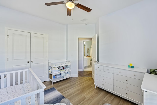 bedroom with ceiling fan, light hardwood / wood-style floors, a crib, and a closet