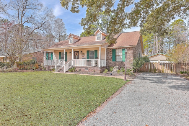 cape cod home with gravel driveway, covered porch, fence, a front lawn, and brick siding