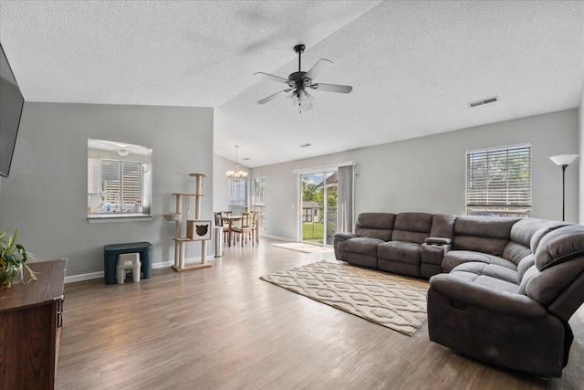 living area with lofted ceiling, ceiling fan with notable chandelier, wood finished floors, and visible vents