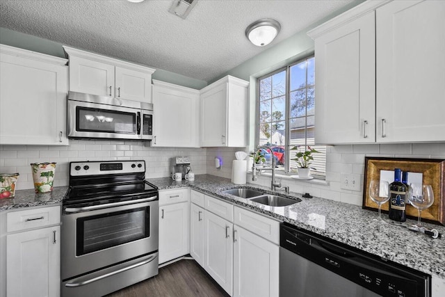 kitchen with visible vents, white cabinets, dark wood-style floors, stainless steel appliances, and a sink