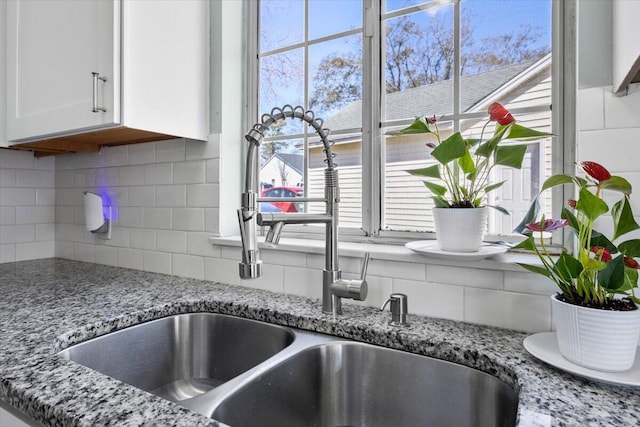 interior details featuring tasteful backsplash, a sink, light stone countertops, and white cabinets