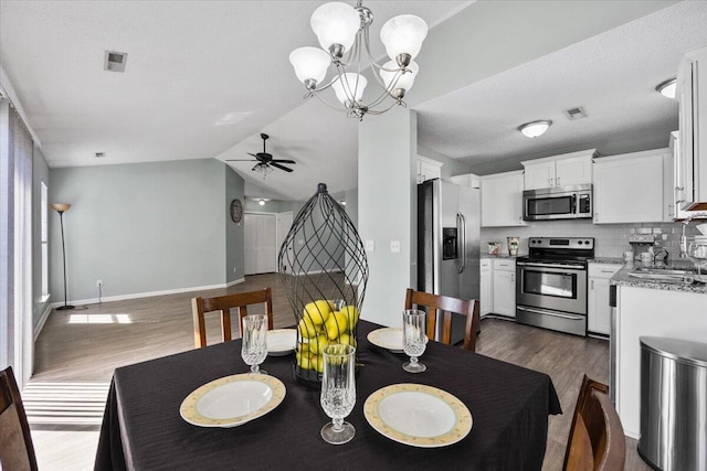 dining space with baseboards, dark wood finished floors, lofted ceiling, stairs, and ceiling fan with notable chandelier