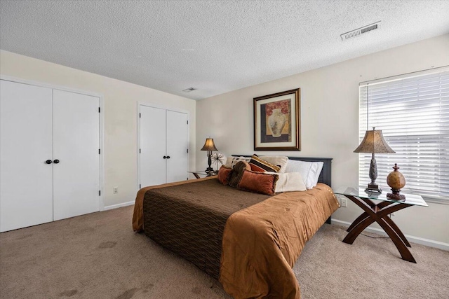 carpeted bedroom featuring baseboards, a textured ceiling, visible vents, and two closets