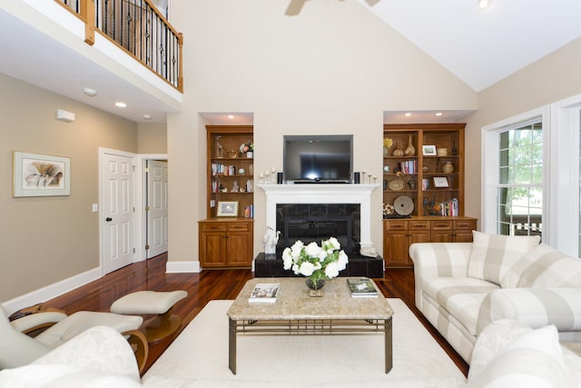 living room featuring dark wood-type flooring, a tiled fireplace, high vaulted ceiling, and built in features