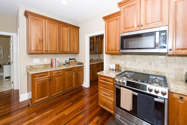 kitchen featuring appliances with stainless steel finishes, decorative backsplash, dark hardwood / wood-style floors, and light stone counters