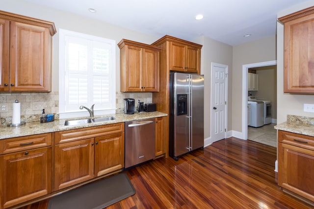 kitchen with washing machine and dryer, sink, stainless steel appliances, light stone counters, and dark hardwood / wood-style floors