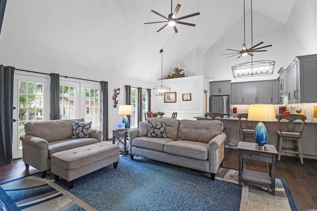 living room with ceiling fan with notable chandelier, dark wood-type flooring, and high vaulted ceiling