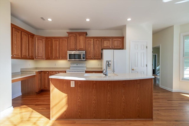 kitchen with a center island with sink, light hardwood / wood-style floors, white appliances, and sink