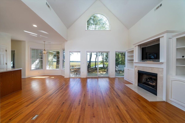 unfurnished living room with built in shelves, light wood-type flooring, and high vaulted ceiling