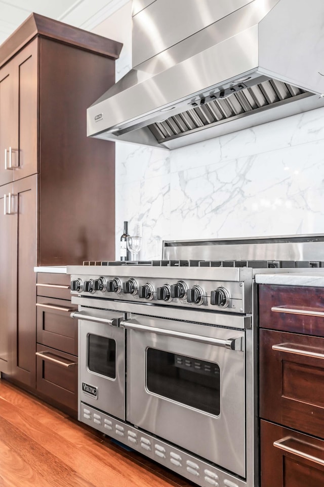 kitchen featuring ventilation hood, dark brown cabinets, light hardwood / wood-style flooring, range with two ovens, and backsplash