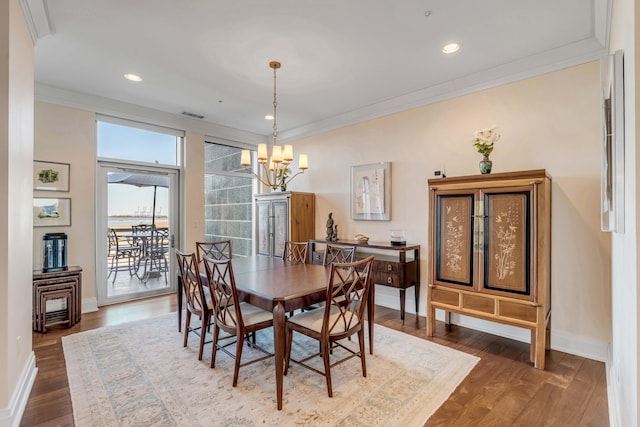 dining area with wood-type flooring, ornamental molding, and a notable chandelier