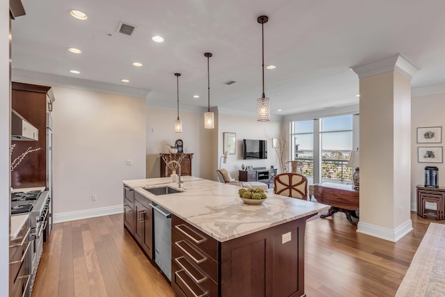 kitchen with sink, light stone counters, ornamental molding, appliances with stainless steel finishes, and a kitchen island with sink
