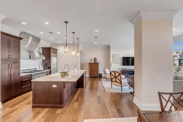 kitchen with sink, an island with sink, pendant lighting, light stone countertops, and exhaust hood