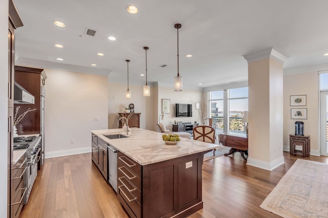 kitchen with decorative light fixtures, sink, ornamental molding, a kitchen island with sink, and light stone countertops