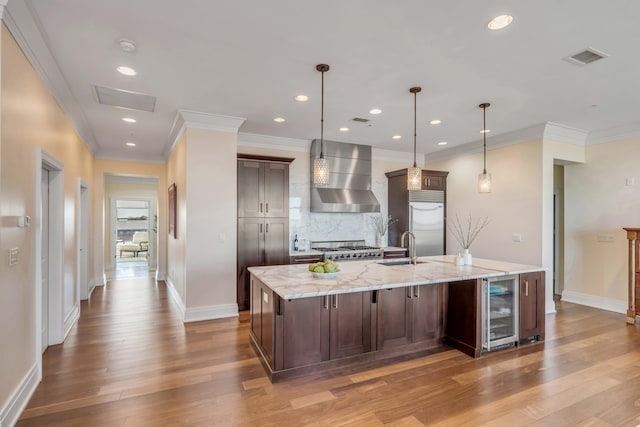 kitchen featuring a spacious island, dark brown cabinetry, stainless steel built in refrigerator, extractor fan, and hanging light fixtures