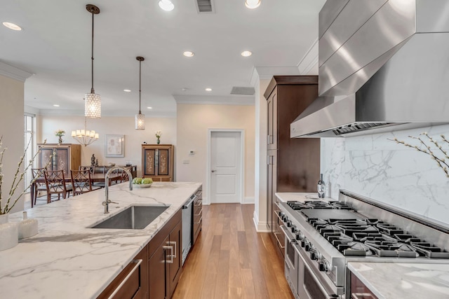 kitchen with wall chimney exhaust hood, sink, appliances with stainless steel finishes, pendant lighting, and light stone countertops